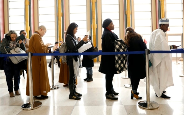 Frauen und Männer warten auf die Registrierung in einer hohen Halle. 