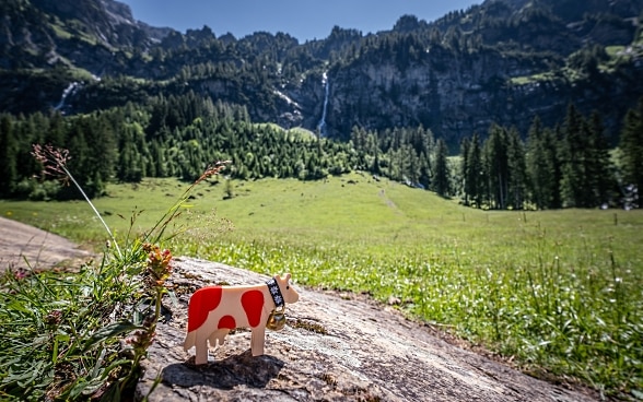 Une vache en bois tachetée de rouge se dresse dans un paysage montagneux suisse.