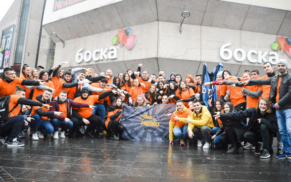 Jugendliche sitzen in einer Gruppe vor einem Gebäude und tragen orange T-Shirts.