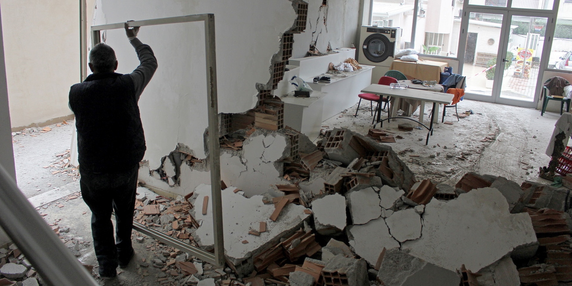 Un uomo sposta il telaio di una finestra all’interno di una stanza distrutta dal terremoto.