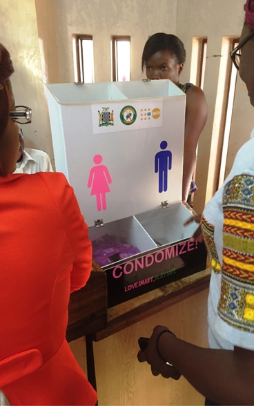 African women holding a discussion next to a box that dispenses contraceptives for women and men.
