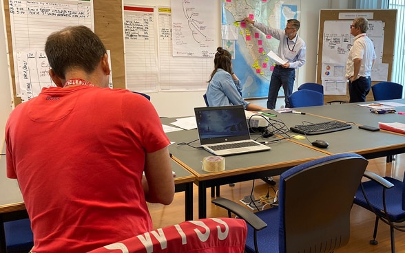 In an office room, embassy staff draw the routes of the buses on posters on the wall. 