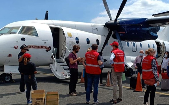  An aircraft stands on the tarmac, passengers and members of the Swiss Embassy stand in front of it.