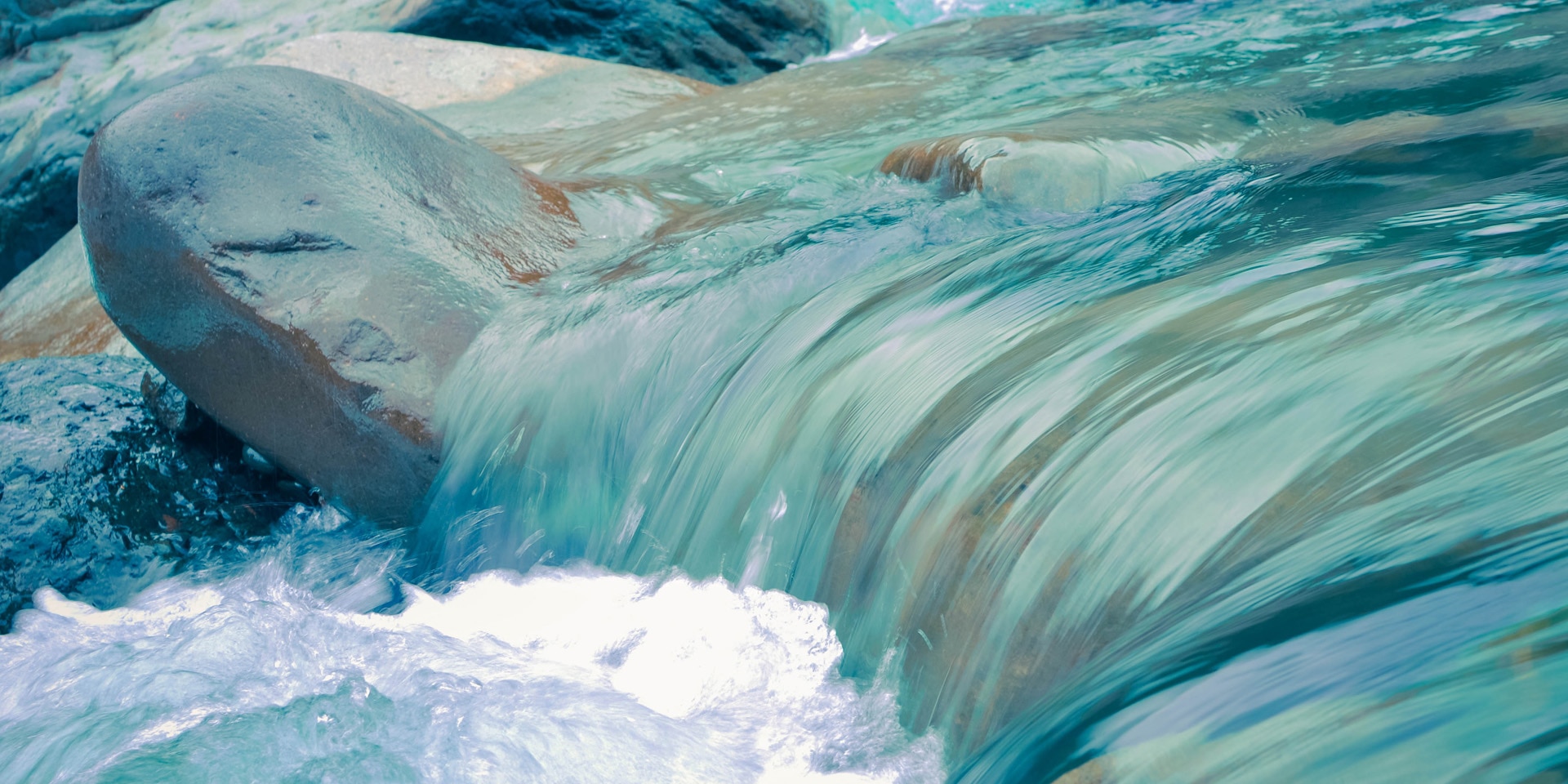 The blue water of a stream ripples over stony terrain.