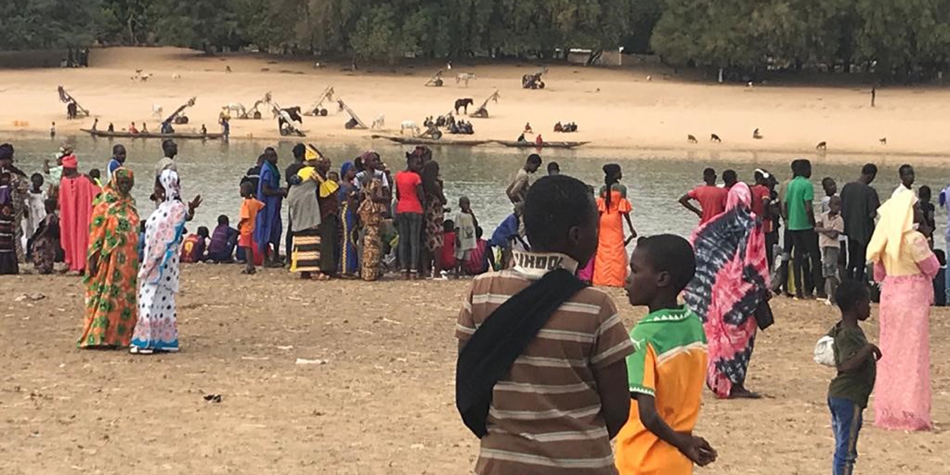 People wearing brightly coloured clothing standing on the bank of the Senegal River which separates Senegal and Mauritania.