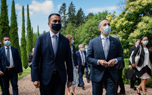 Il consigliere federale Cassis e il ministro degli Esteri italiano Di Maio discutono mentre passeggiano con le loro delegazioni in un parco.