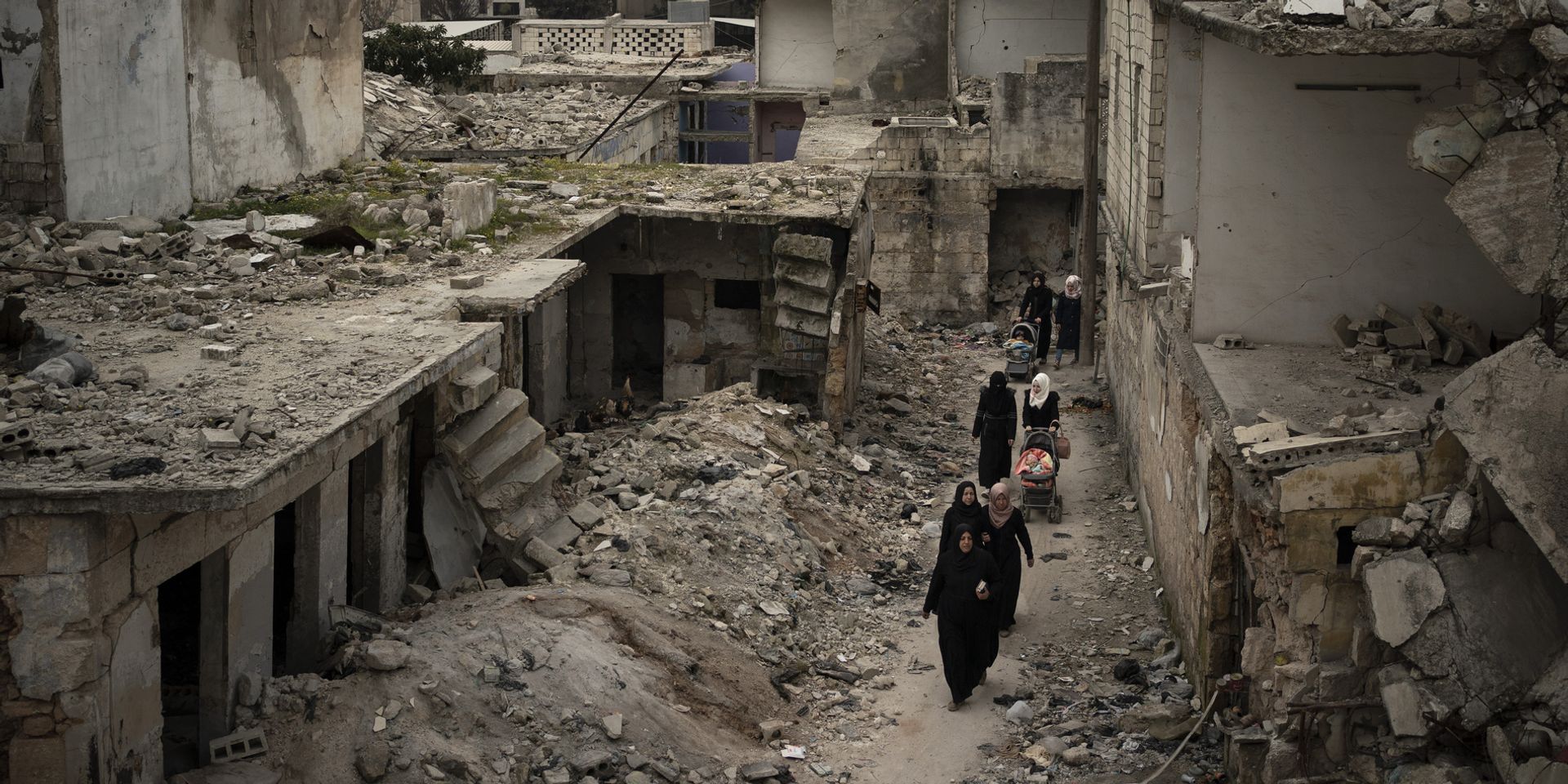  Des femmes marchent avec des poussettes à travers les décombres d'une rue aux maisons effondrées. 