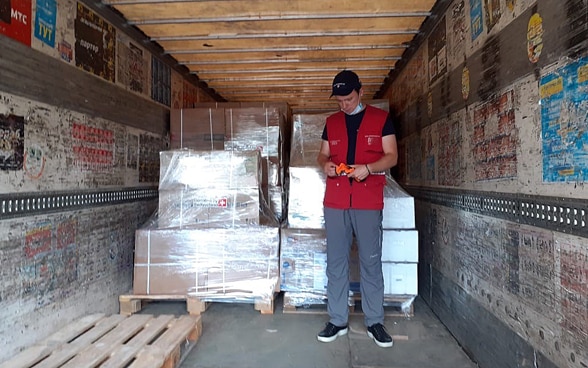  Un homme se tient à l'intérieur d'un camion, devant des palettes d'aide humanitaire. 