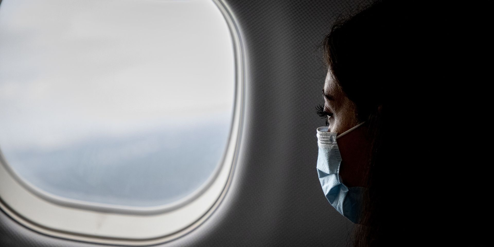 A woman with a face mask is looking out the airplane window.