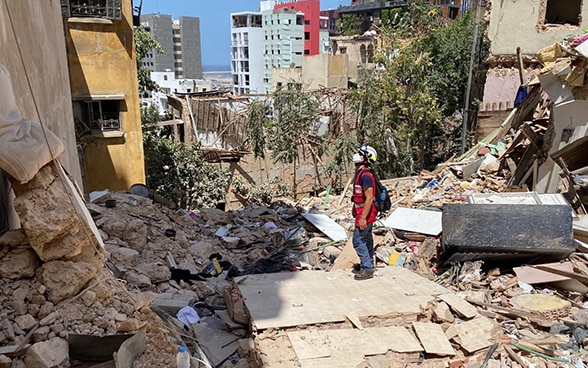 Un expert du Corps suisse d'aide humanitaire se tient devant une maison détruite et entourée de débris.