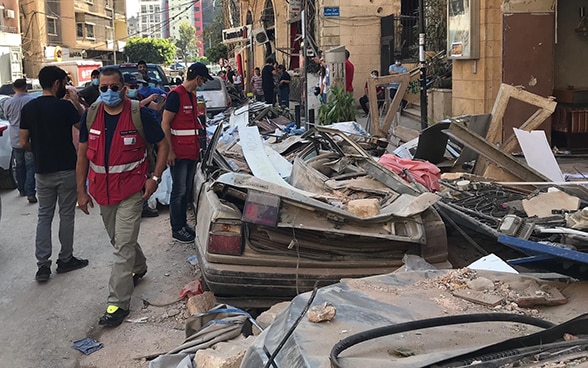 Two experts from the Swiss Humanitarian Aid Unit walk past a demolished car.