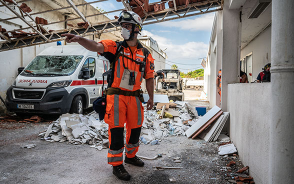 Un expert de l'Aide humanitaire suisse se tient devant les décombres d'un hôpital.