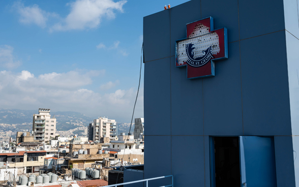 Vista dell'esterno di un ospedale distrutto. Sullo sfondo si vedono le conseguenze dell'esplosione sulla città di Beirut.