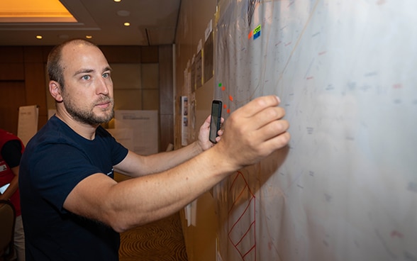 An expert from the Swiss Humanitarian Aid Unit is standing in front of a plan hanging on a wall.