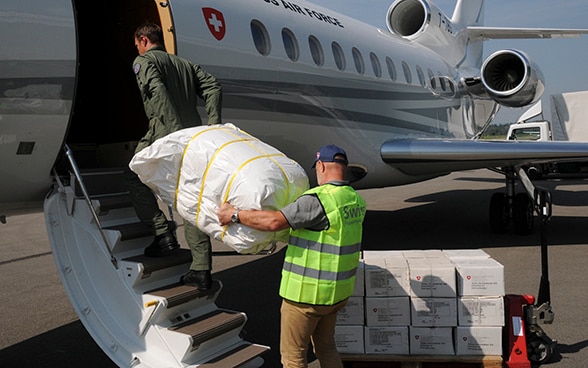 Zwei Männer tragen ein Paket mit Hilfsgütern ins Flugzeug.