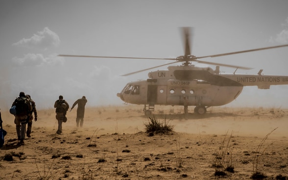  People running towards a UN helicopter landing in a dusty field in central Mali