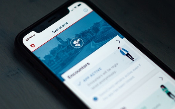 Un smartphone, posé sur une table, révèle la page d’accueil de l’application SwissCovid.