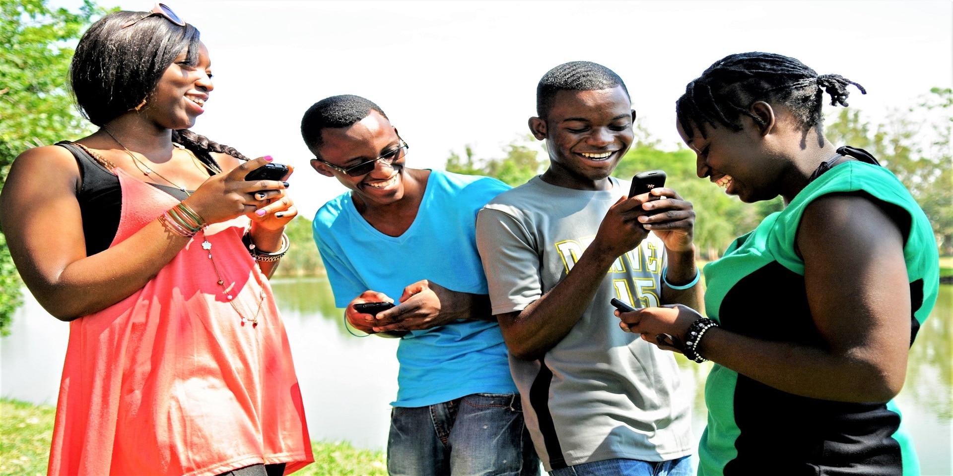 Quattro giovani in primo piano sorridono guardando gli schermi dei loro cellulari.