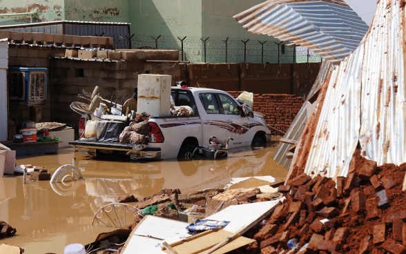 Accanto ai detriti di un’abitazione, un’automobile è carica di mobili recuperati dal fango.