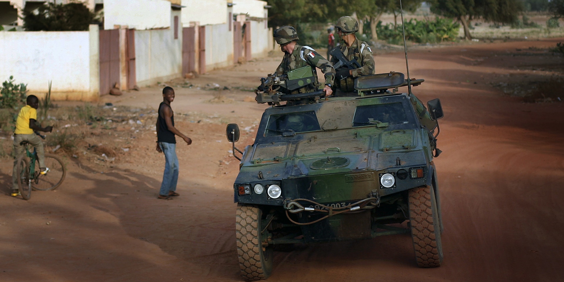 Un veicolo militare che trasporta due soldati passa davanti a dei giovani in una zona di conflitto del Mali.  