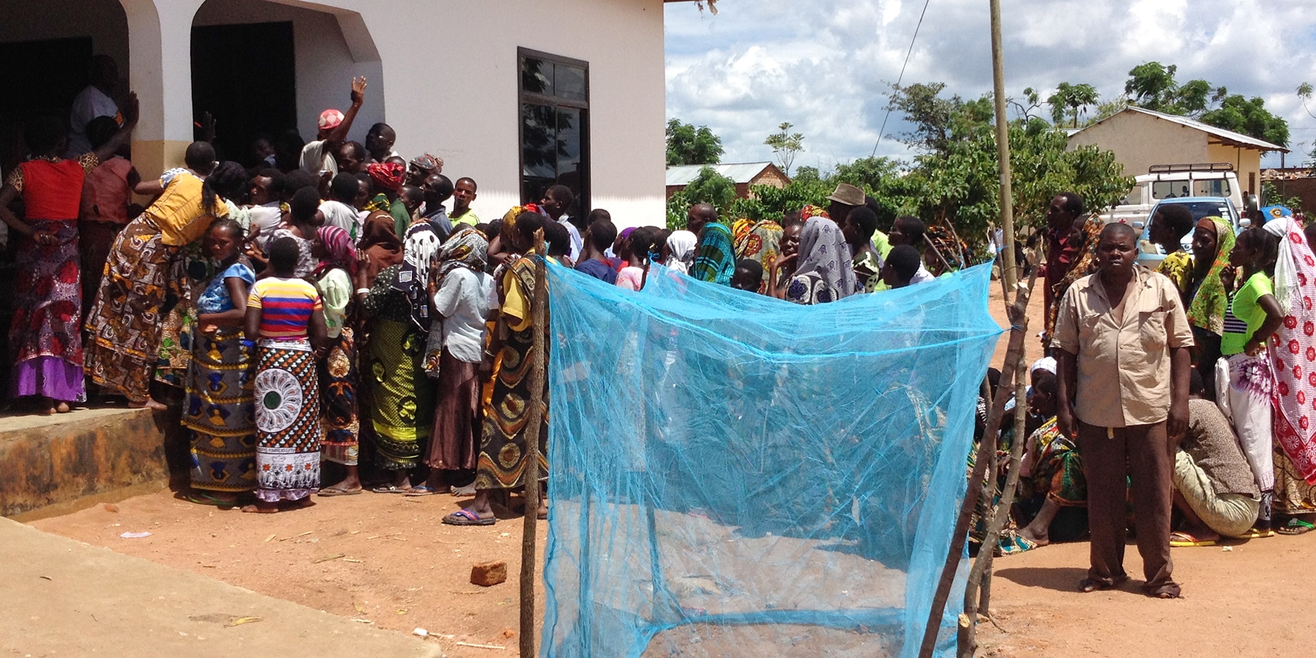 Varias personas en fila van a recoger mosquiteras en un pueblo de Tanzania. Mosquitera azul en primer plano. 