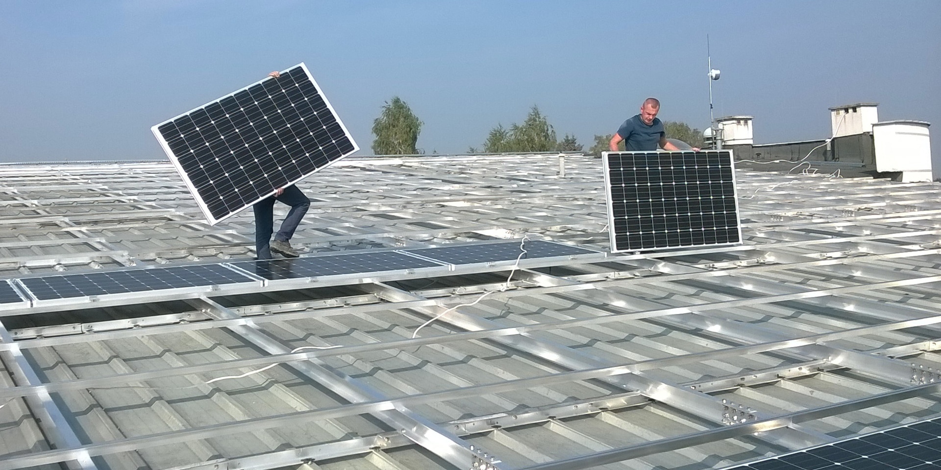 Two technicians install solar panels on the roof of a public building.