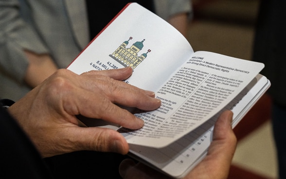 Bundesrat Ignazio Cassis blättert in dem kleinen Buch. Seine Hände, die das Buch öffnen, sind im Vordergrund zu sehen.