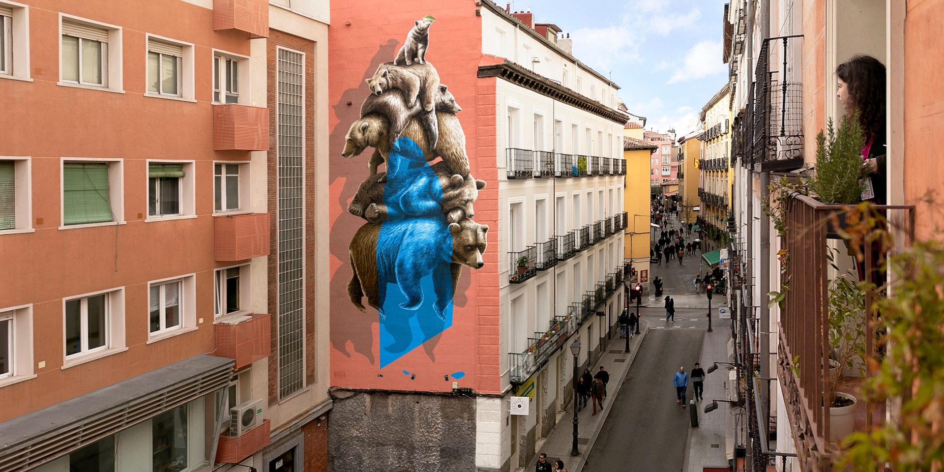 Das Nevercrew-Wandbild befindet sich in einer Strasse im Zentrum von Madrid. Eine Frau betrachtet das Bild interessiert von ihrem Fenster aus.