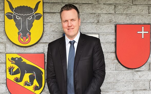 Pascal Sollberger in front of the coats of arms of the cantons of Bern, Schwyz and Uri. 