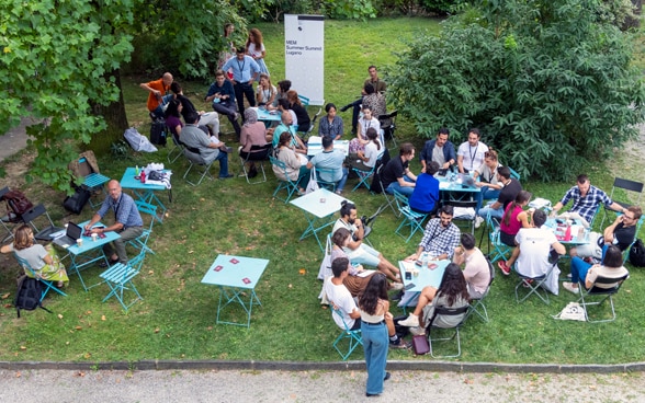 Dans une prairie, des jeunes gens discutent assis autour de tables.