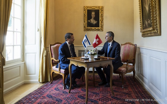 An einem Tisch sitzend, diskutieren Bundespräsident Ignazio Cassis und der israelische Präsident Isaac Herzog.