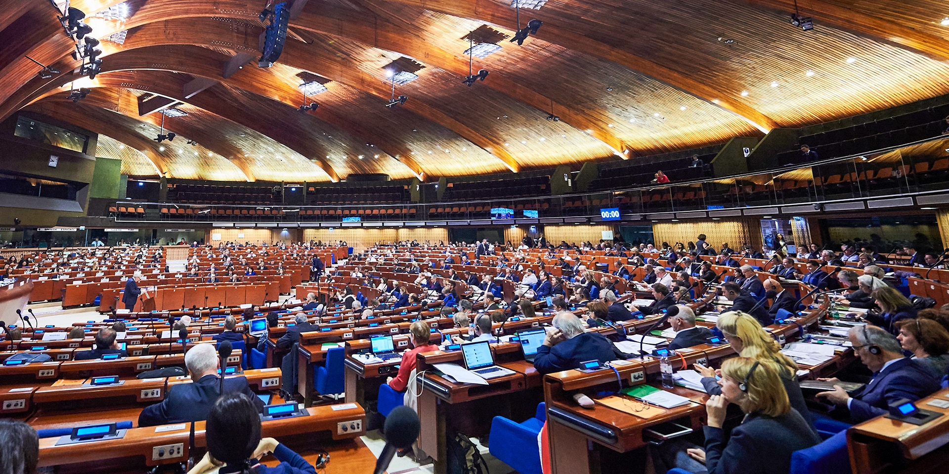 A large hall with a wooden roof construction and rows of seats in a semicircle where the members of the Council of Europe’s Parliamentary Assembly sit.