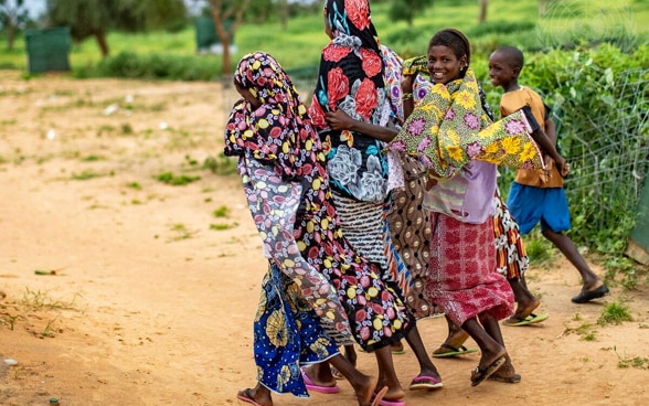 Una donna e dei bambini africani camminano lungo una strada polverosa.