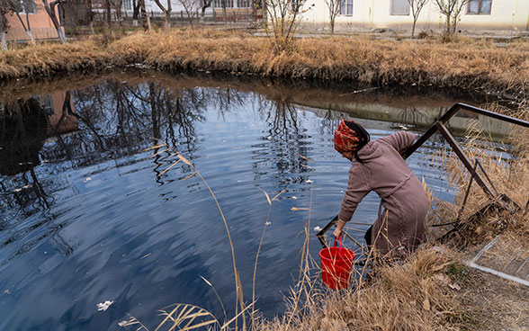 Una ragazza con una sciarpa rossa attinge acqua con un secchio.