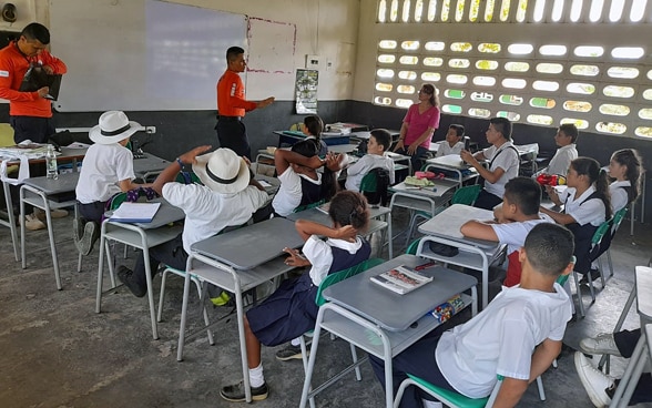 Experts standing in a classroom teaching schoolchildren about mine risks.