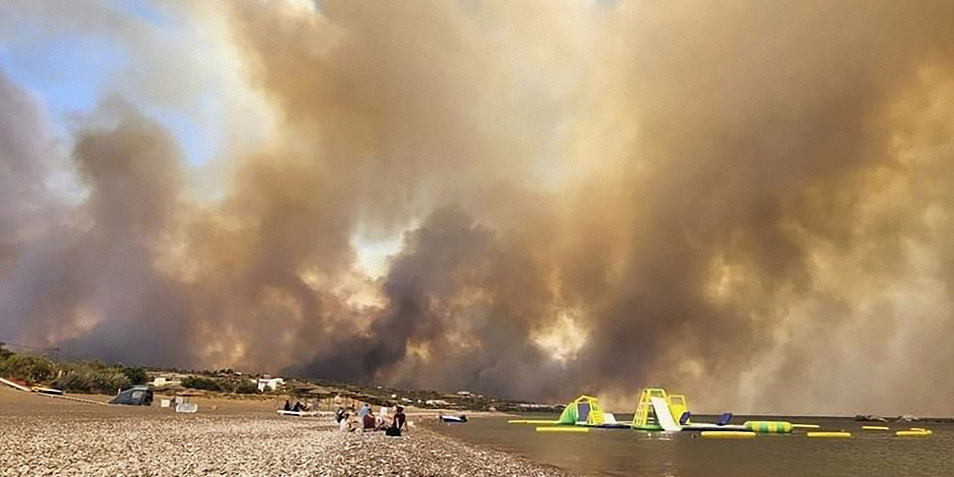 A pebble beach with slides and air mattresses, with thick clouds of smoke rising above.