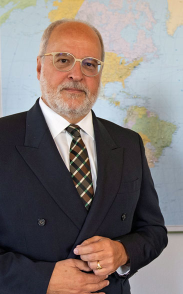 Portrait of State Secretary Alexandre Fasel. A world map hangs on the wall behind him.