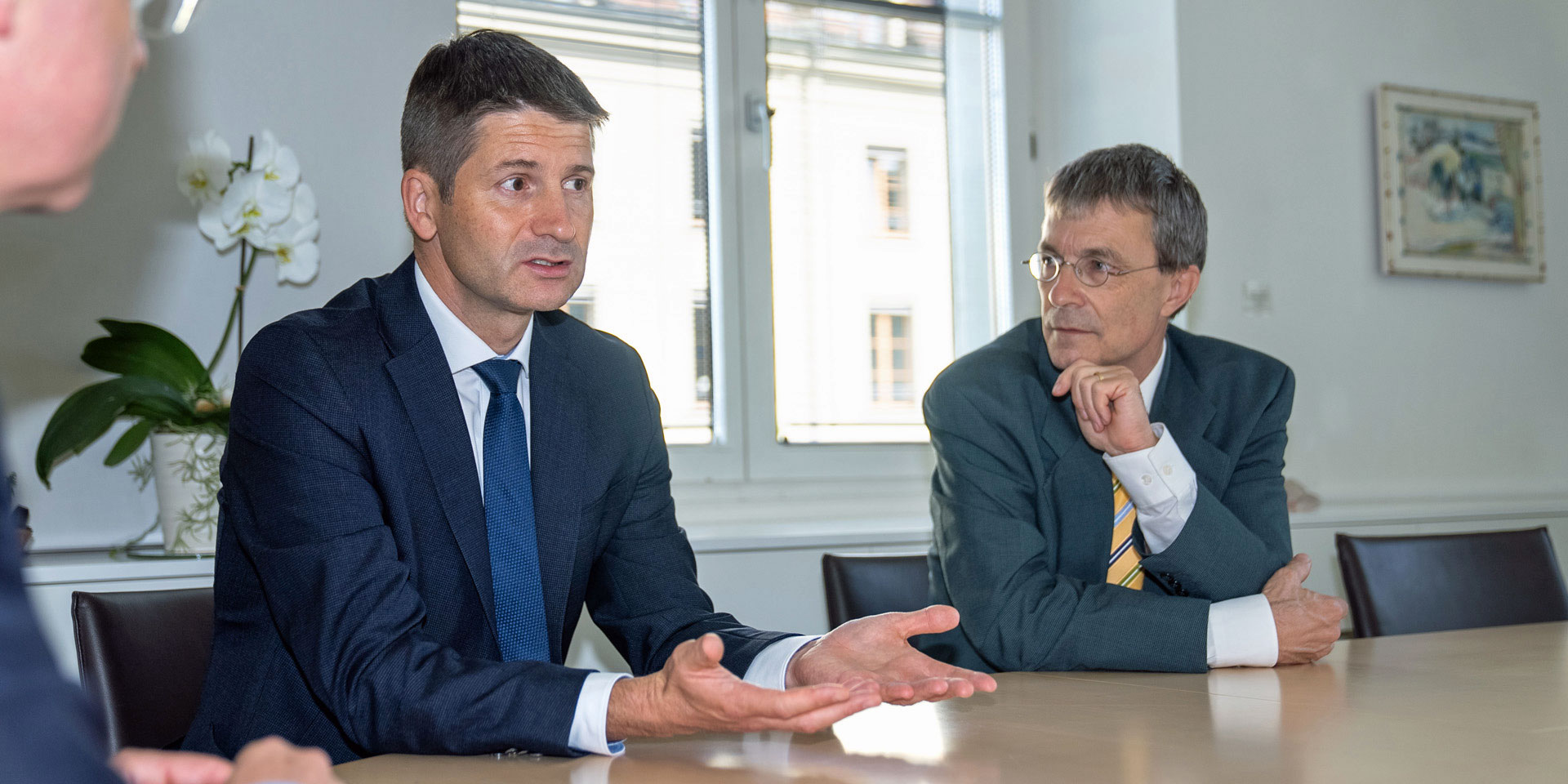 Gabriel Lüchinger is talking at a table. Franz Perrez, seated to his right, is listening to him.