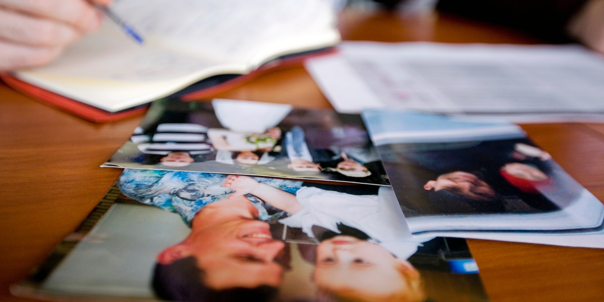 Family photos are placed on a table with a person filling in an ICRC form in the background.