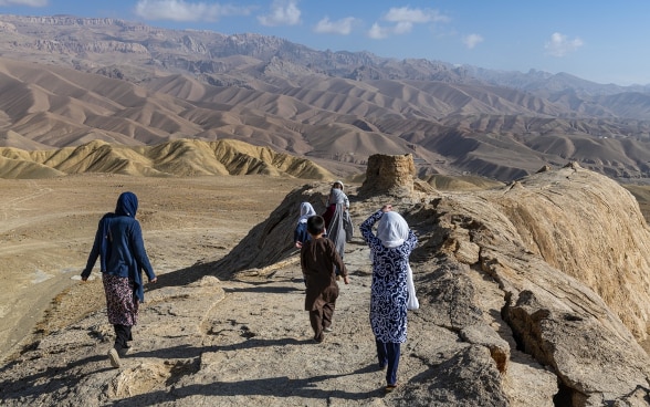 In a barren mountainous landscape in Afghanistan, four girls and a boy walk along a ridge.