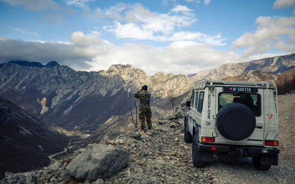 Un membro dell'Esercito svizzero osserva con un binocolo una valle in Bosnia ed Erzegovina.