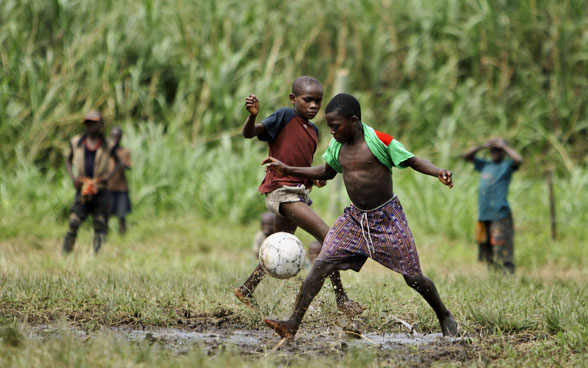 Des enfants congolais jouent au football sur une pelouse dans une zone rurale.