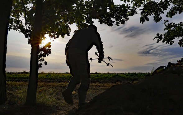 A man carries a drone down the slope of a small hill.