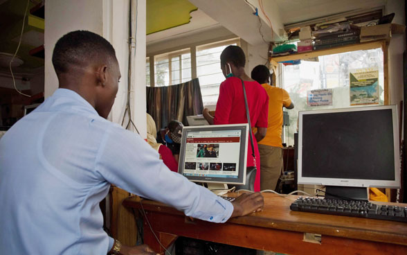 An African man sits behind a computer reading a newspaper online.