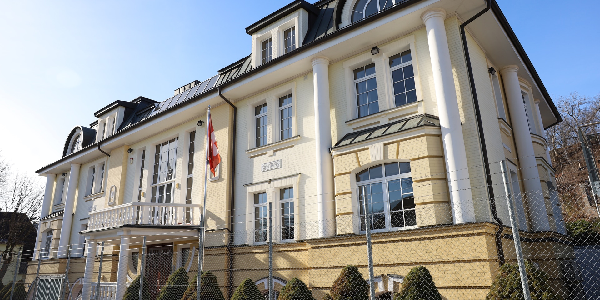 Une maison à la façade peinte en jaune clair, devant laquelle se trouve un drapeau suisse.