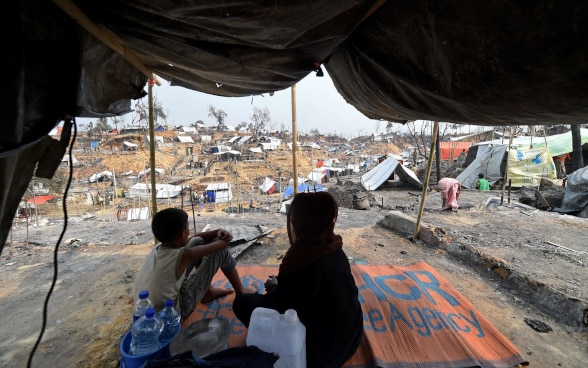 A woman and a child are seen against the backdrop of temporary shelters set up for displaced Rohingya refugees.