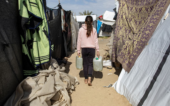 Una ragazza palestinese trasporta due contenitori d'acqua in una tendopoli per sfollati interni a Gaza.
