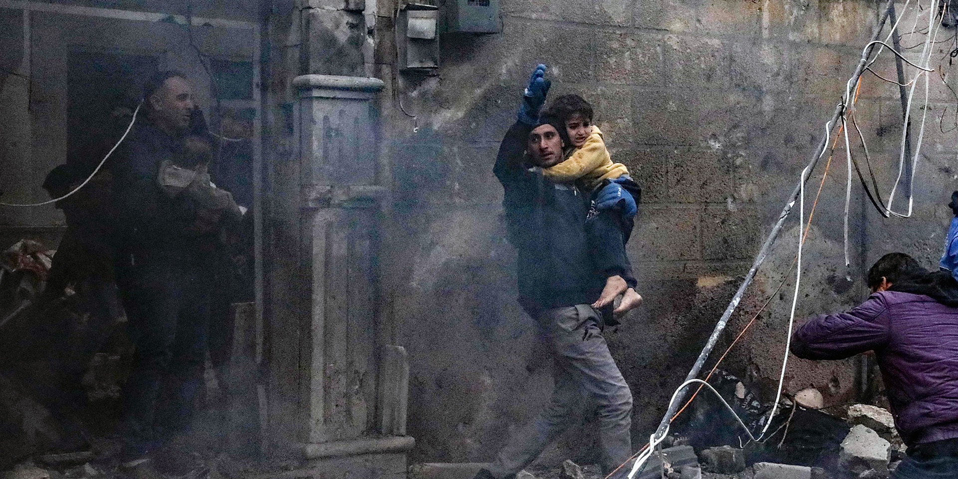 Ein Mann hält inmitten von Trümmern in Syrien ein Kind in den Armen.