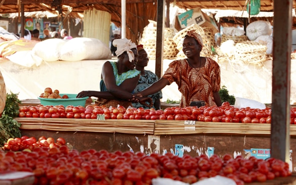 Two women behind a market stall in Uganda filled with ripe tomatoes.