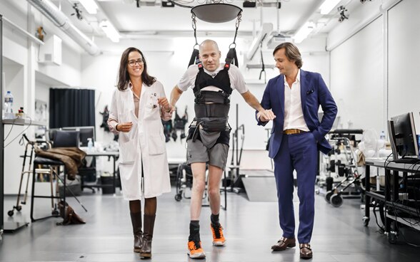Die Professoren Jocelyne Bloch und Grégoire Courtine gehen mit dem Paraplegiker Sebastian Tobler durch einen Raum in einer Forschungseinrichtung.